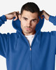A blue hooded sweatshirt features a full zip and is modelled by a man adjusting the hood. It has a logo.