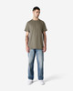 A model stands wearing a plain olive green Gildan Ultra Cotton adult T-shirt paired with light blue jeans.