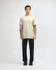 A unisex short sleeve T-shirt in beige, paired with black cargo pants, featuring a logo on the shirt.