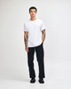 A young man wearing a plain white unisex short sleeve t-shirt and loose blue jeans, standing against a white background.