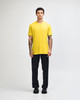 A model wearing a yellow unisex short sleeve T-shirt with black cargo pants and green and white shoes, featuring a logo.