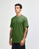 A unisex CVC short sleeve t-shirt in green, shown on a model standing sideways. Features a logo on the garment.