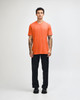 A model wearing an orange unisex CVC short sleeve t-shirt paired with black cargo trousers and sneakers.