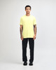 A man wearing a bright yellow unisex short sleeve t-shirt and black baggy pants, with sneakers.
