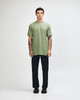 A model wearing a green unisex short sleeve T-shirt and black cargo pants, standing in a neutral setting.