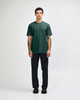 A green unisex CVC short sleeve T-shirt displayed on a model wearing black cargo pants and sneakers.