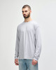 A long sleeve grey t-shirt displayed on a model wearing dark pants and white sneakers, featuring a logo.