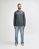 A man wearing a long sleeve grey t-shirt paired with light blue jeans and black sneakers. The shirt has a logo.