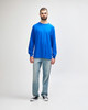 A man wearing a blue long sleeve T-shirt and light blue jeans, standing against a neutral background.