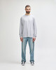 A grey long sleeve T-shirt worn by a man standing against a plain background, paired with light blue jeans.