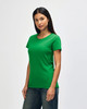 A woman wearing a green Gildan Heavy Cotton ladies' T-shirt, paired with blue jeans against a plain background.