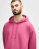 A pink hooded sweatshirt with a drawstring, featuring a hood and a simplistic design, is displayed on a model.