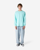 A unisex long sleeve t-shirt in a light aqua colour, paired with loose-fit blue jeans and black sneakers.