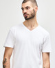 A man wears a white Gildan Softstyle adult v-neck t-shirt, with a logo on the shirt. He smiles while posing.