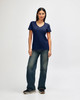 A woman is wearing a navy Gildan Softstyle ladies' V-neck T-shirt, paired with blue jeans and white sneakers.