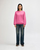 A woman in a pink Gildan Softstyle adult sweatshirt and blue jeans, adjusting her sleeve. The sweatshirt has a logo.