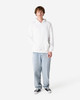 A unisex hooded sweatshirt in white, featuring a front pocket and a plain design. The model wears casual light blue jeans.