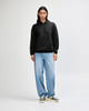 A unisex black hooded sweatshirt is worn with light blue baggy jeans and black sneakers, featuring a logo.
