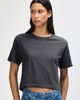 A woman models a grey boxy T-shirt with short sleeves and a relaxed fit, paired with light denim jeans.