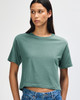 A woman wearing a teal boxy t-shirt, styled with light blue denim shorts. The shirt has a logo.