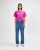 A boxy women's T-shirt in vibrant magenta, paired with light blue wide-leg jeans. The model stands with hands on hips.