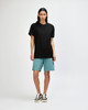 A person wearing a black unisex pique mockneck t-shirt paired with teal shorts and black sneakers, standing against a neutral background.
