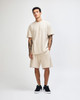 A model stands in a beige unisex mockneck T-shirt and matching shorts, paired with black footwear.