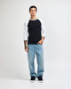 A unisex raglan T-shirt with a black body and white three-quarter sleeves, paired with light blue jeans and black sneakers.