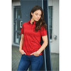 A red women's polo shirt featuring a collar and short sleeves, displayed on a model against a modern backdrop.