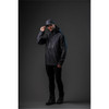 A man wearing a black Men's Patrol Softshell jacket and cap, standing against a dark background. The jacket has a logo.