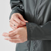 A close-up of a person's hands adjusting the cuffs of a dark grey wind jacket. The jacket features a zipper and has a logo.