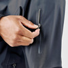 A close-up of a hand unzipping a pocket on a black rain jacket. The jacket features a sleek design and has a logo.