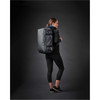 A woman wearing black activewear carries a grey Equinox 30 Duffel Bag on her back against a dark background.