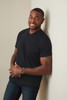 A man wearing a black classic V-neck T-shirt, standing against a wall with a friendly smile.