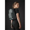 A quilted dark green backpack is worn on the back of a model in a black outfit, showcasing its sleek design.