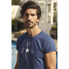 A blue crew neck t-shirt featuring a simple logo design, modelled by a man near a pool.