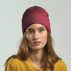 A maroon beanie worn by a model with long hair, paired with a yellow top, featuring a branding logo.