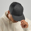 A grey trucker cap with a solid front and mesh back, worn by a person in a cream hoodie.