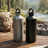 A drink bottle set in grey and black, featuring a carabiner, placed on a wooden surface near a stream.