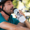 A drink bottle with a black cap, featuring a logo, is held by a man wearing a helmet and teal shirt.
