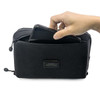 A black toiletry bag with a hand placing a phone inside, featuring a logo on the front.
