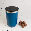 A reusable coffee cup in vibrant blue with a black lid, alongside a few chocolate-covered treats.