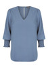 A blue Cleo V Neck shirt with long, puffed sleeves and smocked cuffs. It features a deep V-neckline and branding.