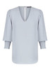 A light blue V-neck shirt with puffed sleeves and smocked cuffs, featuring a back slit detail. It has a logo.