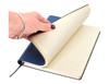 A hand holding a blue A5 notebook with lined pages, featuring a smooth cover and a ribbon bookmark.