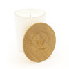 A large white glass candle with a wooden lid, featuring a logo and an embossed design on the lid.