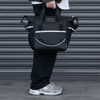 A cooler bag in black with strap and handles, featuring a logo, held by a person near a grey backdrop.