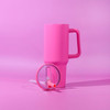 A pink tumbler with a handle and straw, featuring a clear lid, set against a pink background.