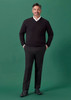 A man wearing a black sweater and black slim fit flat front pants stands against a green background.