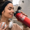 A drink bottle in gradient red with a black lid, featuring a logo. A person is holding it close to their face.